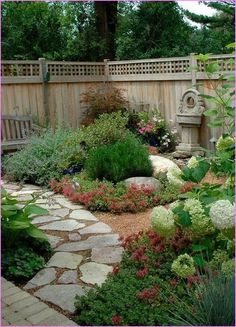 a garden with lots of flowers and plants around it, along with a wooden fence