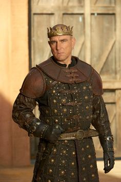 a man dressed in medieval clothing standing next to a wooden door and wearing a crown