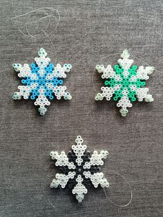 three snowflakes made out of beading on a gray tablecloth, one is blue and the other is green