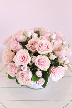 a white vase filled with pink roses on top of a table