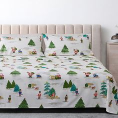 a bed covered in white and green christmas themed bedspreads with trees on them