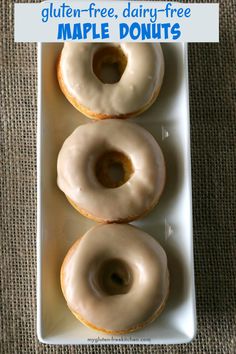 three glazed doughnuts on a white plate sitting on a brown cloth covered table