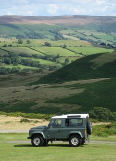 a jeep is parked on the side of a road in front of rolling green hills