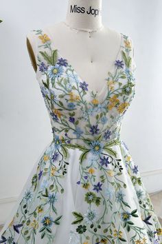 a white dress with blue and yellow flowers is on display in front of a mannequin