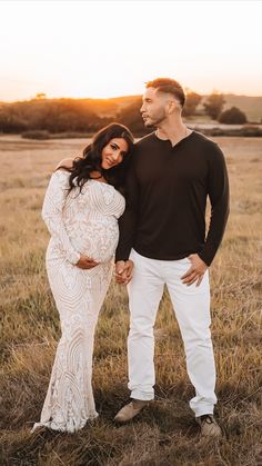 a pregnant couple standing in the grass at sunset