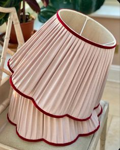 a pink lamp shade sitting on top of a table next to a potted plant