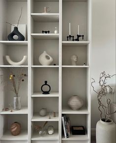 a white shelf with vases and other items on it's shelves in a living room