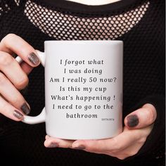 a woman holding a white coffee mug with black writing on it