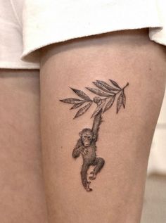 a woman's thigh with a tattoo of a monkey hanging from a tree branch