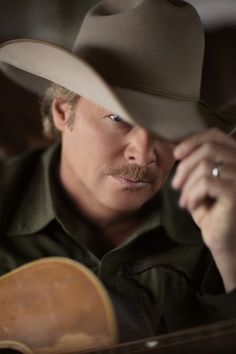 a man wearing a cowboy hat and holding a guitar in his right hand while looking into the distance