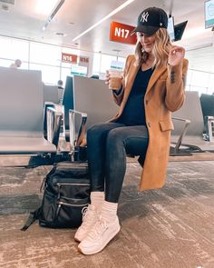 a woman sitting on top of a luggage bag in an airport with her hand up