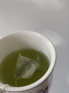 a cup filled with green liquid and a paper boat floating in the water next to it