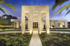 the entrance to a modern home at night with palm trees in front and lights on