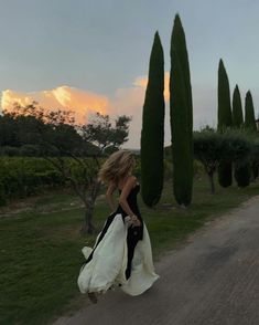 a woman is walking down the road with her dress blowing in the wind as the sun sets