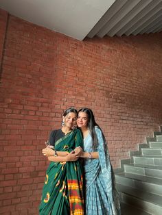 two women standing next to each other in front of a brick wall with stairs behind them