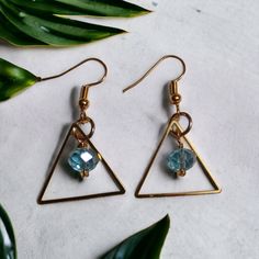 Recently worn by actress Rosa Arredondo in her role as Francey on the hit show, "So Help Me Todd", these stunning Gold Triangle Earrings, feature a mesmerizing Aquamarine glass faceted drop.  These earrings are truly an experience with golden, geometric, stainless triangles reflecting the light and capturing attention with every movement. The Aquamarine glass drop, in a beautiful, oceanic blue is the heart of these earrings, symbolizing tranquility, clarity, and elegance.  Treat yourself to the Faceted Teardrop Crystal Earrings For Parties, Metal Earrings With Faceted Beads, Gold Crystal Earrings With Faceted Beads, Metal Earrings With Faceted Beads For Party, Faceted Crystal Earrings For Party, Glass Faceted Beads Earrings For Gift, Glass Earrings With Faceted Beads As A Gift, Glass Earrings With Faceted Beads For Gift, Faceted Dangle Jewelry For Party