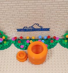 an orange plastic vase sitting on top of a white floor next to a flower covered wall