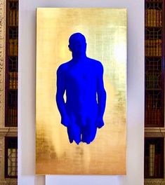 a blue man standing in front of a gold wall with bookshelves behind it