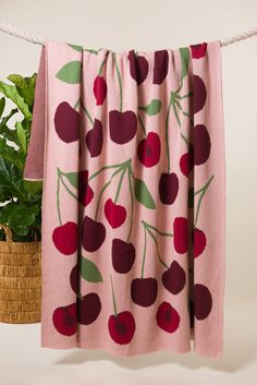 a pink blanket with cherries on it hanging from a rope next to a potted plant