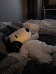 a teddy bear laying on top of a bed with headphones in its mouth,