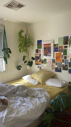 an unmade bed in a bedroom with posters on the wall and a cat sleeping on it