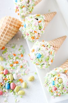 three ice cream cones filled with sprinkles and candy eggs on a white plate