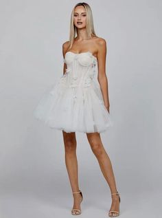 Embrace your inner romantic with this White Strapless Sweetheart Neck Corset Floral Appliqué Layered Tulle Mini Dress. This dreamy mini dress features a strapless sweetheart neckline, beautifully highlighting the décolletage for a feminine and elegant look. The corset bodice, with its tie-back detail, cinches the waist, offering a flattering silhouette and structured fit. Intricately designed floral appliqués adorn the bodice, adding a touch of whimsy and elegance. Layers of soft tulle create a Spring Cocktail Corset Dress In Tulle, Strapless Tulle Mini Dress For Wedding, Feminine Mini Corset Dress For Wedding, Feminine Mini Length Corset Dress For Wedding, Feminine Mini-length Corset Dress For Wedding, Sheer Organza Mini Dress, White Coquette Mini Dress For Party, Spring Strapless Tulle Corset Dress, Strapless Tulle Corset Dress For Spring