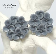 pair of blue flower shaped earrings on white sculpture with hand holding it up to the side