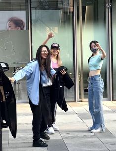 two women standing on the sidewalk with their arms in the air and one woman holding her hand up