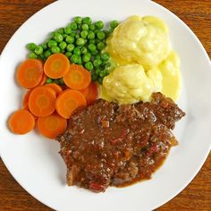 a white plate topped with meat, mashed potatoes and carrots next to peas