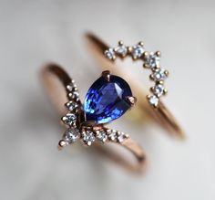 two gold rings with an oval shaped blue sapphire and small white diamonds on each ring