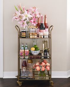 a gold bar cart filled with bottles and flowers on top of a hard wood floor