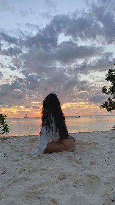 a woman is sitting on the beach at sunset