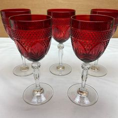 four red glass goblets sitting on top of a white cloth covered tablecloth