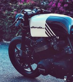 a black and white motorcycle parked in front of some bushes with purple flowers behind it