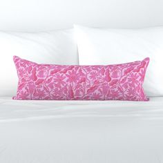 a bed with white sheets and pink flowers on the pillow case, along with two pillows