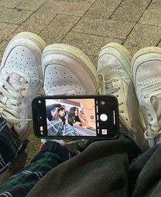 someone taking a photo with their cell phone while sitting in front of two pairs of shoes