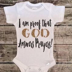 a white bodysuit with gold lettering that says i am proof that god loves me