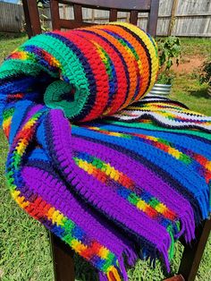 a multicolored crocheted blanket sitting on top of a wooden chair in the grass