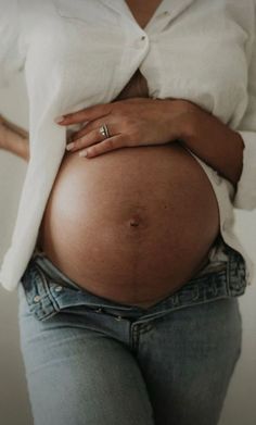 a pregnant woman wearing jeans and a white shirt is holding her belly in the air