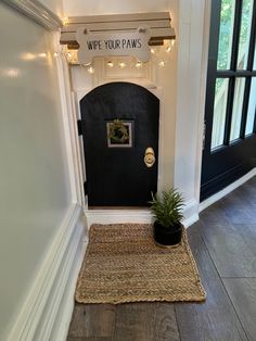 a black door with a sign that says wipe your paws and a potted plant