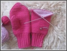 a pair of pink mittens sitting on top of a white blanket next to yarn