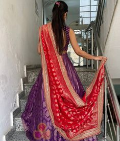 a woman in a purple and red sari walking down stairs with her hand on the railing