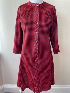 "Vintage 60s shift dress by Lady Mendel Knits of Distinction, no size tag. Red and black plaid print, button up front. Long sleeve, thick polyester feel. Two chest pockets, slightly flared skirt with two pleats. Missing bottom button, slight repair needed along collar and left chest pocket. Please ask questions!  Measurements (laid flat):  Length: 40\" Pit to Pit: 18\"x2 Waist: 18\"x2 Hips: 22\"x2 Condition: Good vintage condition, left pocket is slightly detached, missing one button (pictured).  The vintage pieces I sell have all led a previous life and may tell their stories through minor imperfections. I'll do my best to indicate overall condition, but please refer to the pictures. Your purchase continues the life of this garment...what stories will you tell while wearing it?  Please no Fitted A-line Plaid Dress For Fall, Retro Plaid Dress For Work, Retro Fitted Knee-length Plaid Dress, Fitted Retro Knee-length Plaid Dress, Fitted Knee-length Retro Plaid Dress, Fitted Button-up Plaid Dress With Buttons, Fitted Button-up Plaid Dress, Fitted Plaid Button-up Dress, Fitted Fall Shirt Dress With Placket