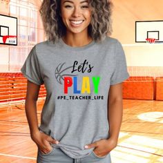 Get ready to hit the playground with our Let's Play Physical Education Teacher Shirt! Designed for energetic educators who love to inspire active play and movement, this shirt is the perfect addition to your PE wardrobe. Made from premium quality fabric, it offers comfort and durability for all your teaching adventures. With its playful design and spirited message, "Let's Play," this shirt encourages fun and fitness in the classroom and beyond. Whether you're leading games, organizing sports act Playful Sports Tops With Letter Print, Elementary Pe Teacher Outfits, School Spirit Letter Print T-shirt, Sporty Graphic Print Tops For Playtime, Sporty Relaxed Fit Tops For School, Sporty Tops For School Sports Season, Pe Teacher, Sporty Crew Neck T-shirt For Playtime, Sporty Graphic Print T-shirt For Playtime