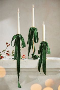 three candles are sitting on a mantle with green ribbons