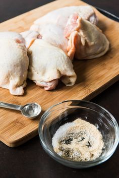 two raw chickens sit on a cutting board next to a bowl of seasoning