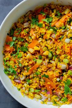 a white bowl filled with corn and vegetables on top of a gray countertop next to a wooden spoon