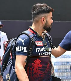 a man with a beard wearing a blue and red shirt is talking to another man