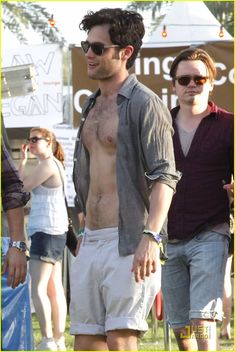 a shirtless man walking in the grass with other people behind him and wearing sunglasses